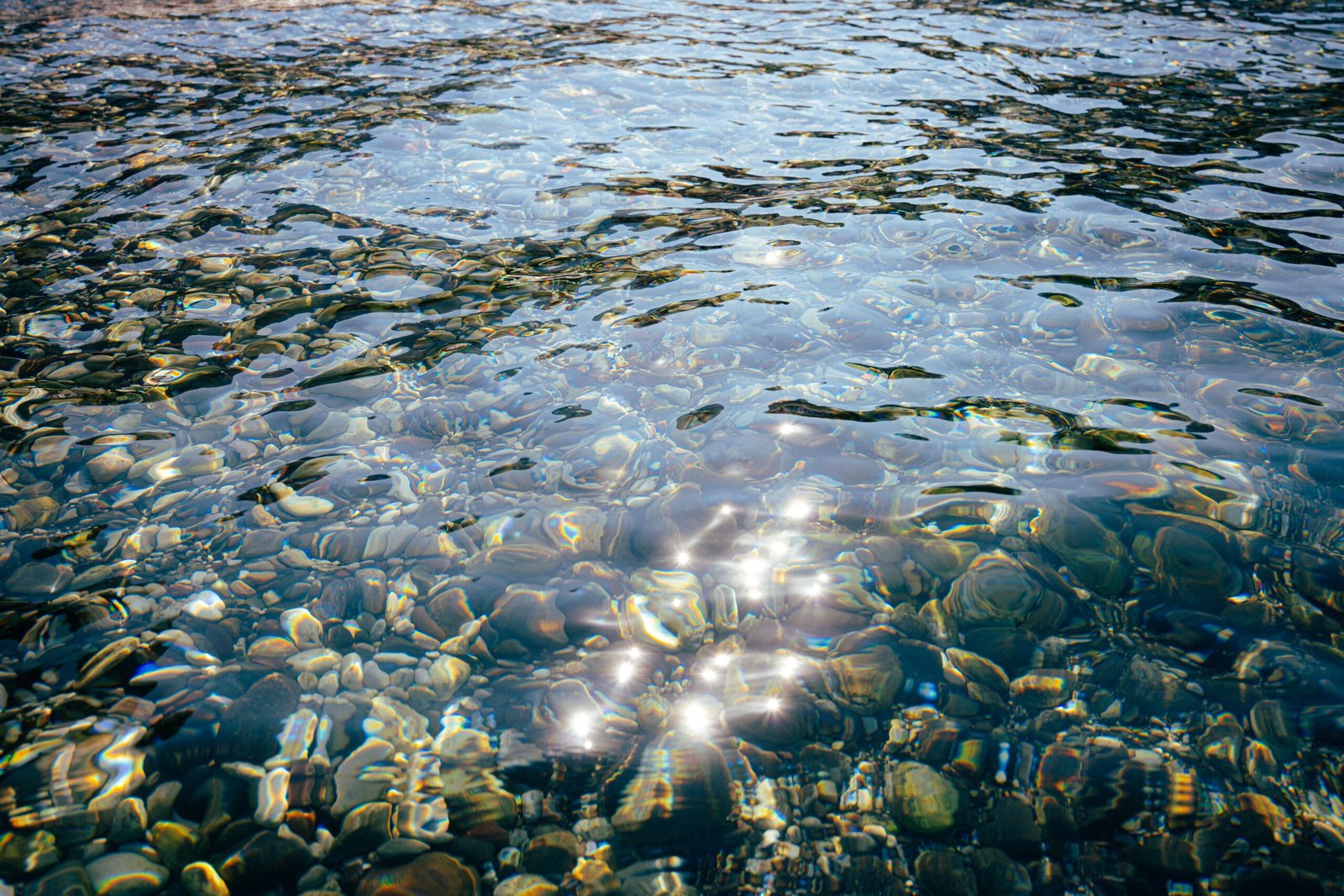 Sunlight sparkles on pebbles under clear water in Marmaris, Türkiye. A vibrant and serene natural scene.
